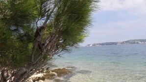A coastal scene with clear shallow waters, a rocky shoreline, and a distant view of a hilly landscape. - LOREDANA KAT by Interhome (Umag)