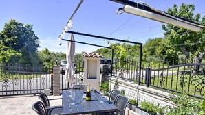 Een terras buiten met een tafel en stoelen, een fles champagne en een decoratieve parasol.