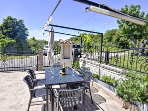 Eine Terrasse im Freien mit Tisch, Stühlen, einer Champagnerflasche und einem dekorativen Sonnenschirm.