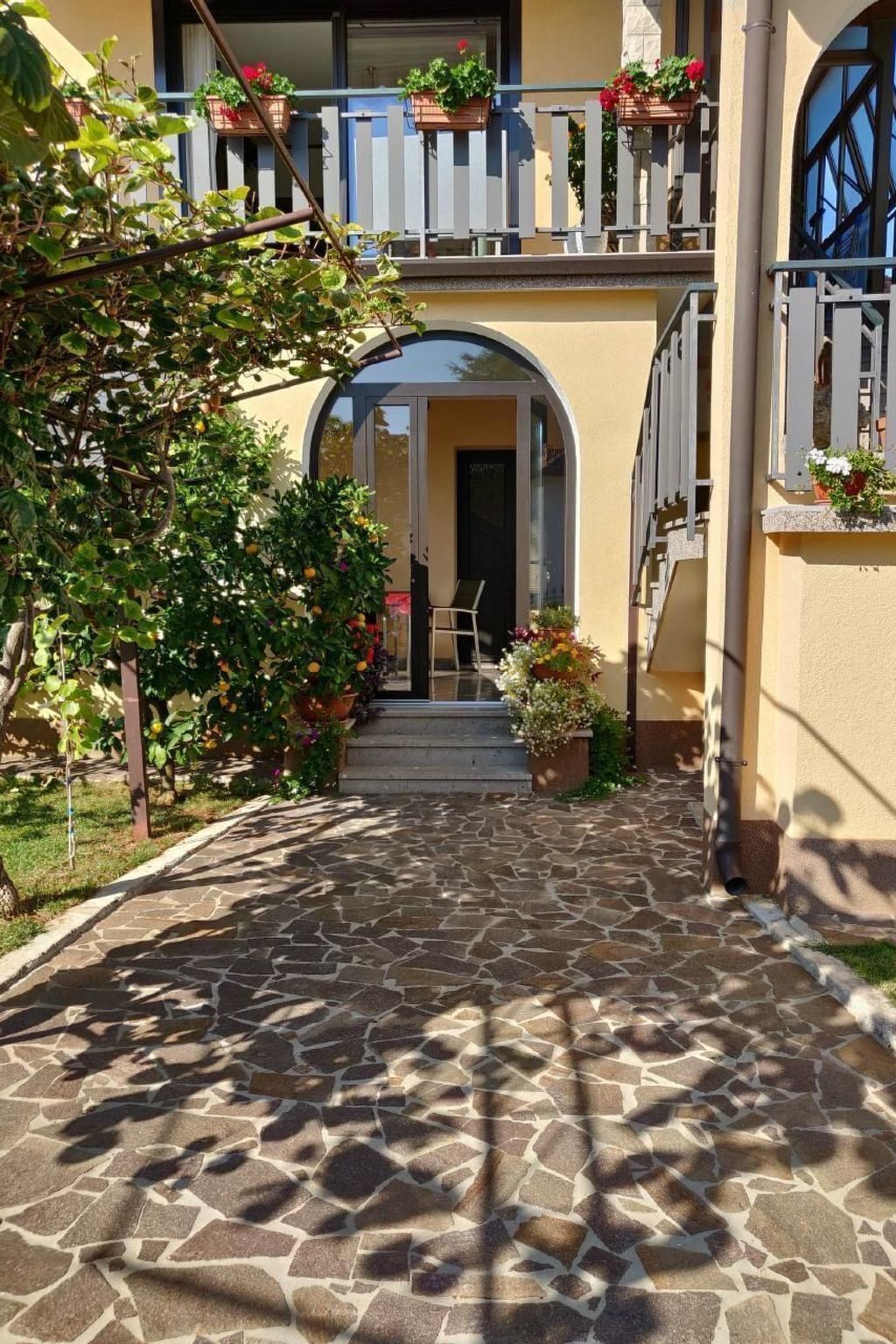 A stone-paved courtyard with a two-story building, arched entrance, and potted plants.