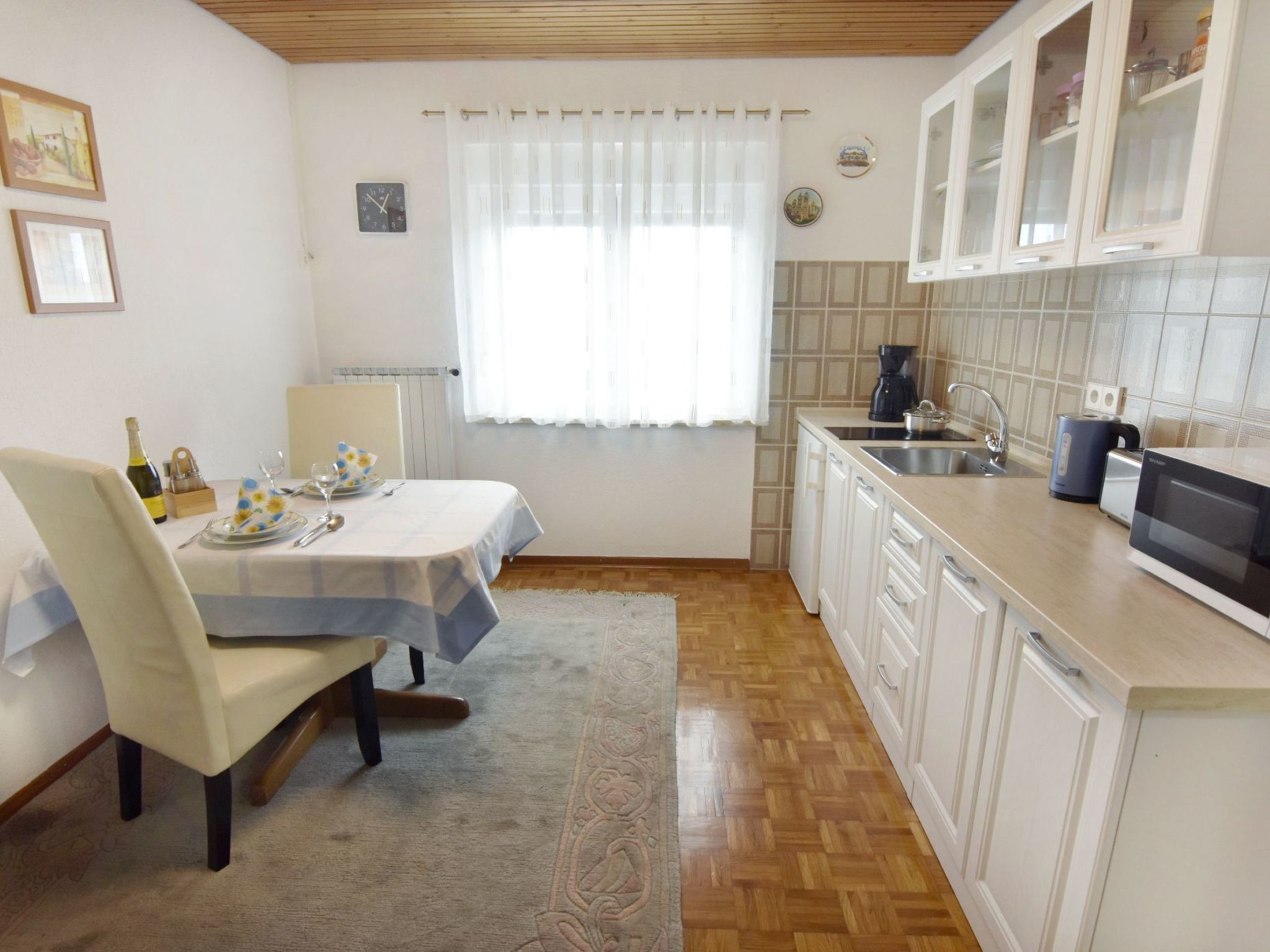 A compact kitchen with white cabinets, a dining table set for two, and a coffee maker.