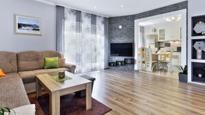 Een moderne woonkamer met een bank, salontafel en televisie. Een eethoek met een tafel en stoelen is zichtbaar door een glazen deur.