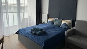 A modern bedroom with a large bed, a grey armchair, and a view through sheer curtains. - Apartment Sky by Interhome (Kolobrzeg)