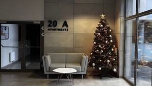 A modern lobby with a sofa and a Christmas tree, a sign indicating 20A apartments, and a view of the city through large windows. - Apartment Sky by Interhome (Kolobrzeg)