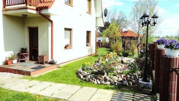 Et toetagers hus med balkon, have med mange planter og et træhegn.