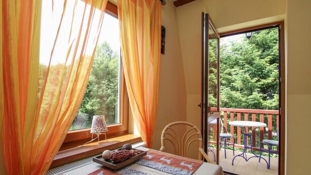 Un balcon avec une table et des chaises, une vue sur la verdure et une fenêtre avec des rideaux.