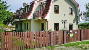 Une maison à deux étages avec un toit rouge, un balcon et une clôture en bois à l’avant.