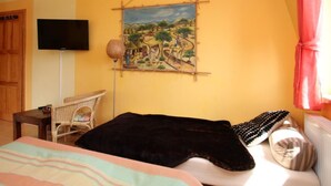 Une chambre à coucher avec un lit, une chaise, un téléviseur et un tableau accroché au mur.