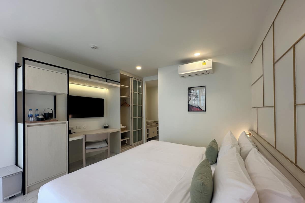 A modern hotel room with a large bed, a desk with a chair, a wardrobe, and a mounted TV.