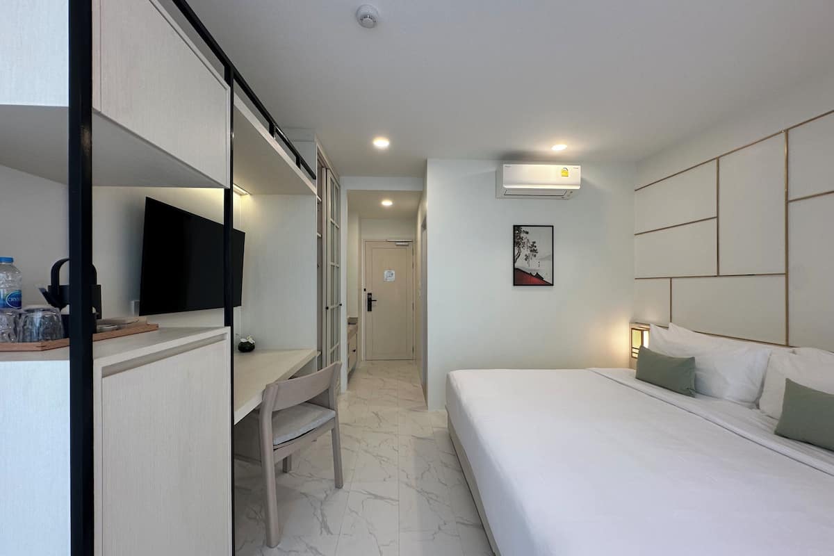 A hotel room with a bed, a desk with a chair, a television, and an air conditioning unit.