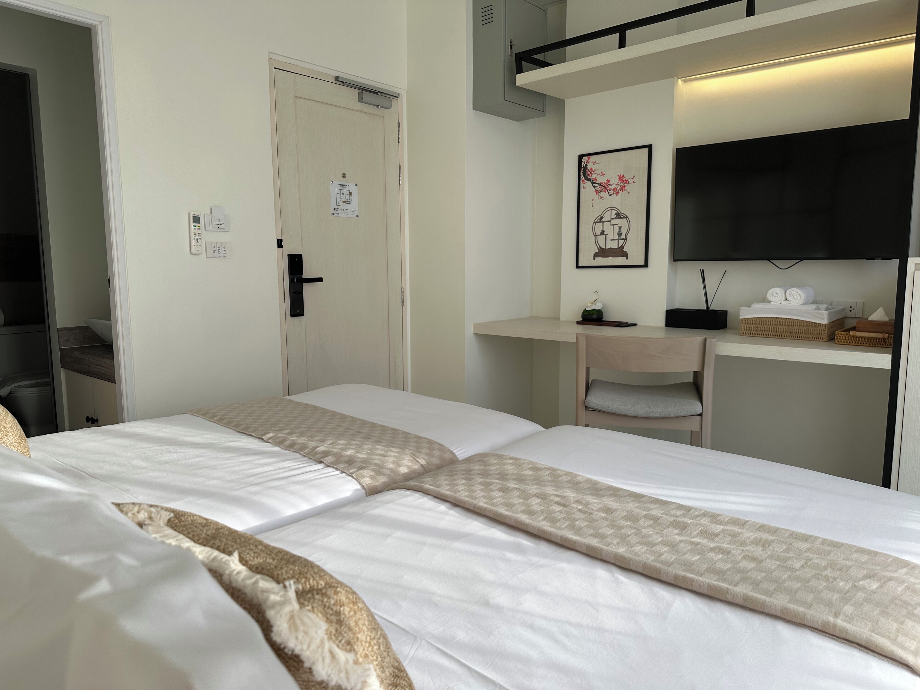 A hotel room with two beds, a desk, a television, and a bathroom visible through an open door.