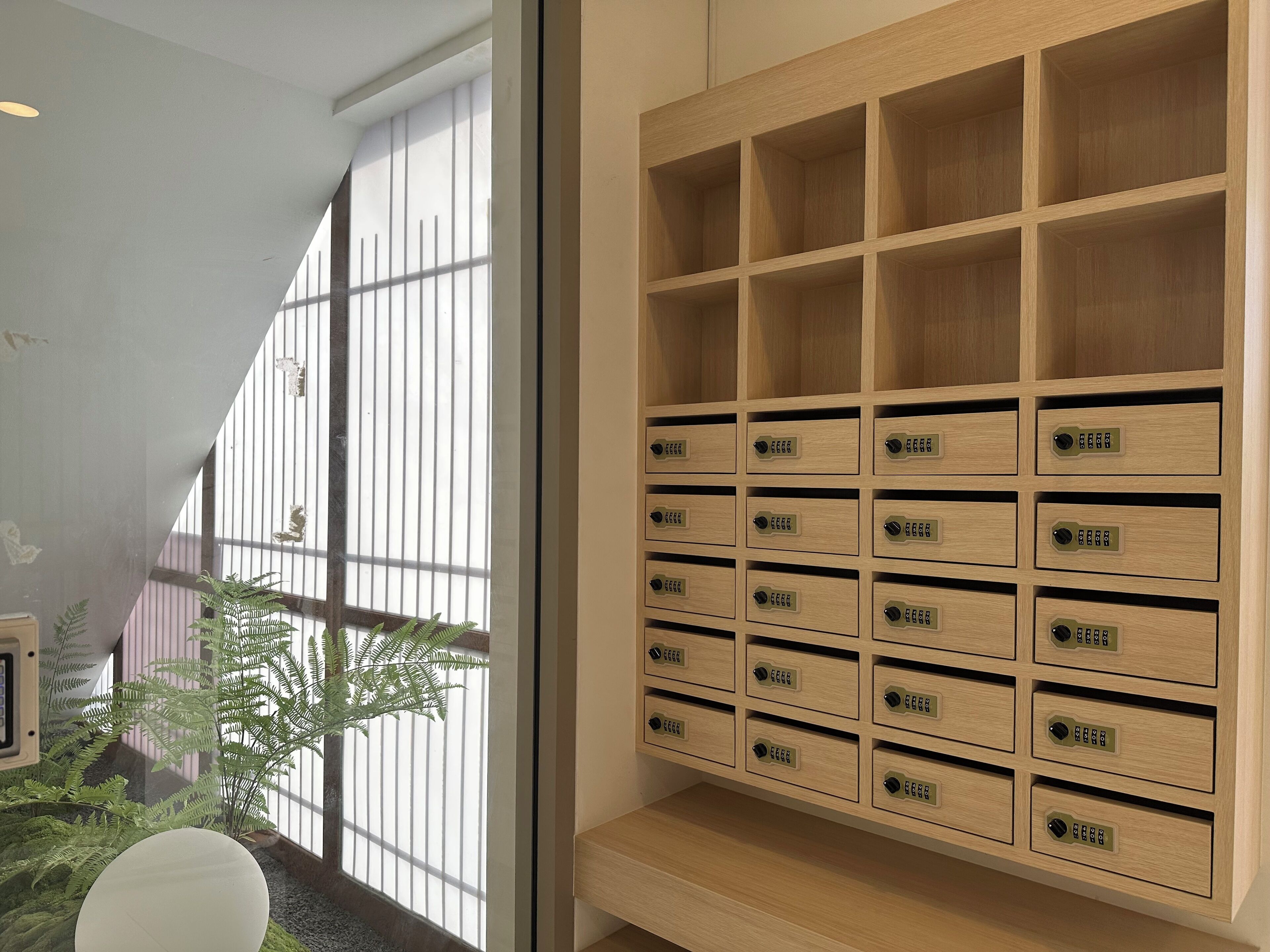 Une chambre moderne dotée d’une grande fenêtre, d’un meuble de rangement en bois comportant plusieurs compartiments et d’une plante en pot.