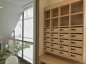 A modern room with a large window, a wooden storage unit with multiple compartments, and a potted plant. - Tatami Hotel Phuket (Kathu)
