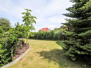Un jardín bien cuidado con diversas plantas, césped y un edificio de techo rojo al fondo.