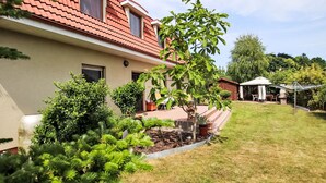 Un immeuble résidentiel avec un toit recouvert de tuiles rouges, une pelouse bien entretenue et une variété de plantes et d’arbustes.
