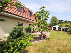 A residential building with a red-tiled roof, a well-maintained lawn, and a variety of plants and shrubs. - Appartement in Rewal mit Grill und Garten by Interhome (Rewal)
