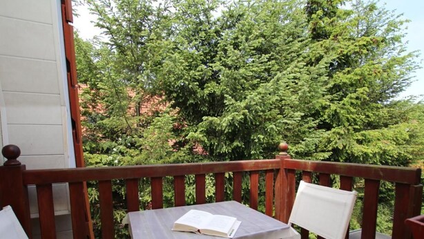 Un balcon en bois avec une table et deux chaises, donnant sur un jardin luxuriant et verdoyant.
