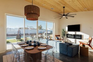 Ein modernes Wohnzimmer mit Essbereich, Sitzgelegenheiten, einem Fernseher und Blick ins Freie.