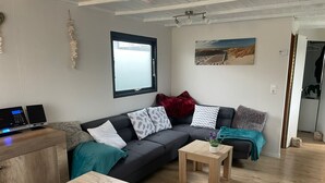 Ein modernes Wohnzimmer mit einem dunkelgrauen Sofa, vielen Kissen, einem kleinen Holztisch und einem wandmontierten Flachbildfernseher.