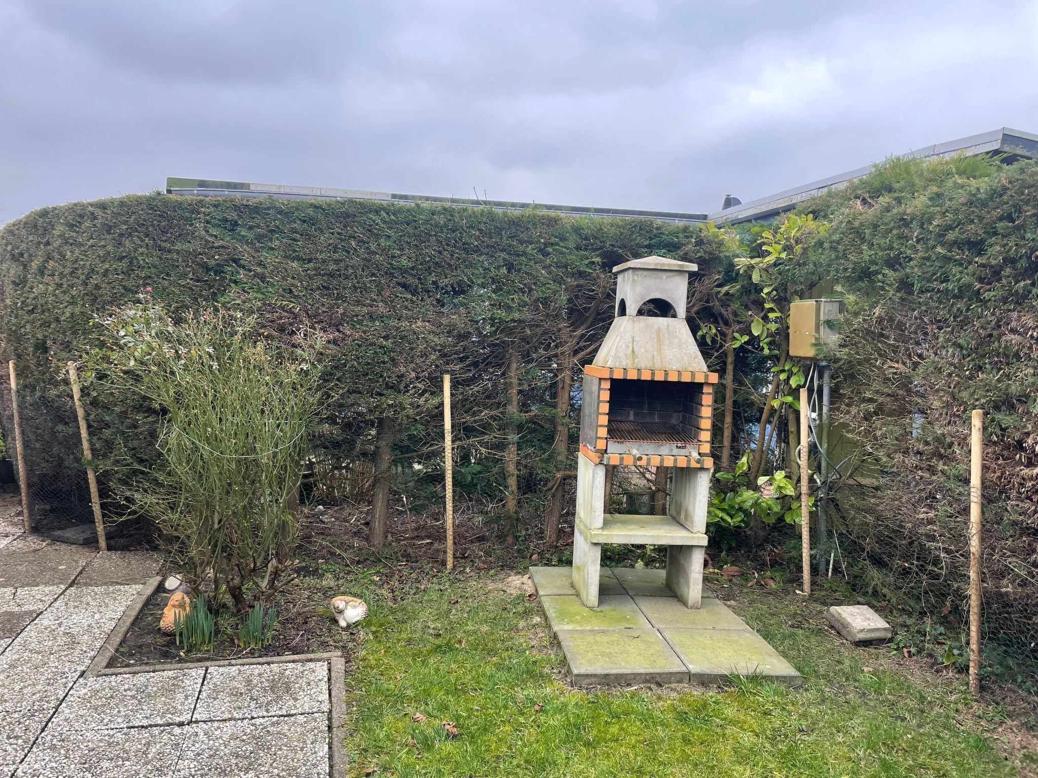 A stone-built outdoor oven with a chimney, surrounded by greenery and a stone pathway.