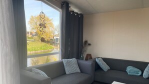 A modern living room with a grey sofa, white cushions, a white coffee table, and a view of a garden through a large window. - Haus Jeff by Interhome (Wervershoof)