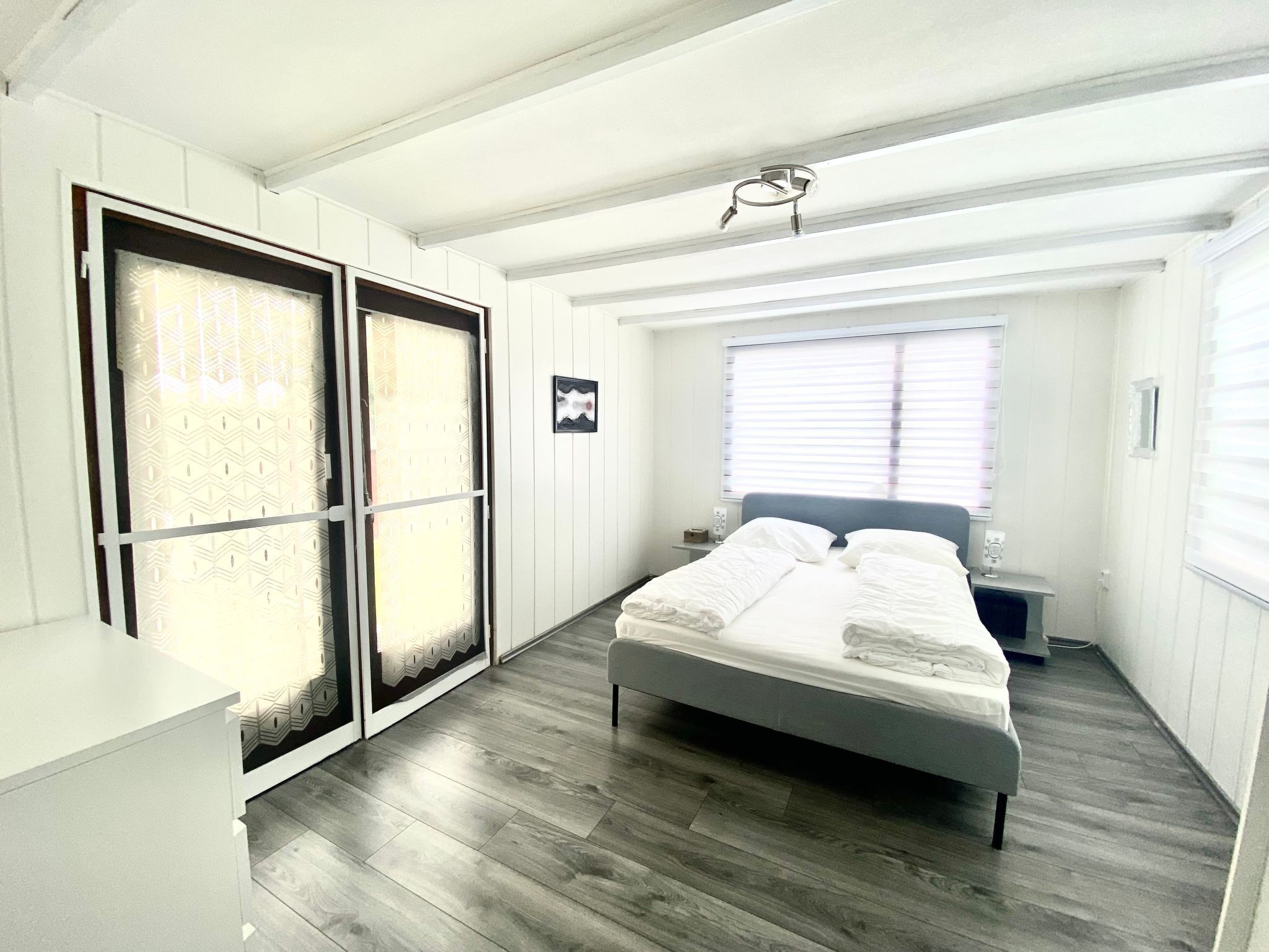 Un dormitorio con cama, mesita de noche, ventana con persianas y puerta con cortina estampada.