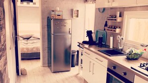A compact kitchen with a refrigerator, oven, and sink. A bed is visible in the adjacent room. - Vacation home  by Interhome (Wervershoof)