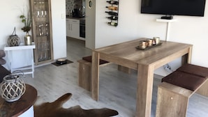 A modern living room with a wooden dining table, benches, a mounted TV, and a wine rack. - Vacation home  by Interhome (Wervershoof)