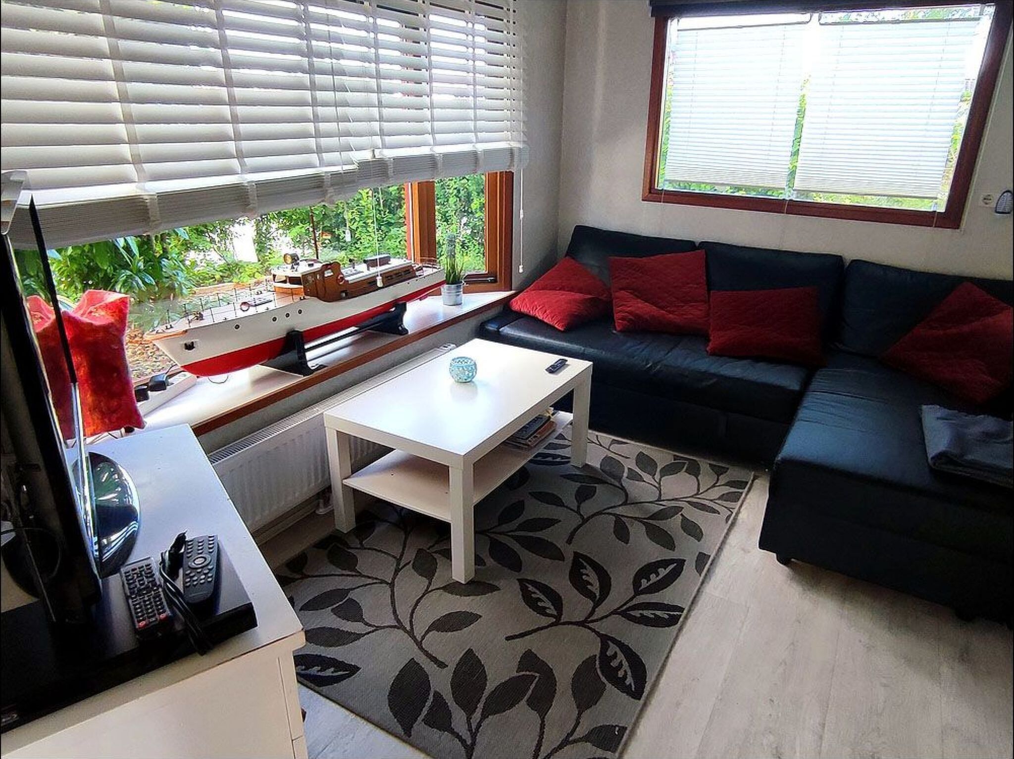 A living room with a sofa, a coffee table, a TV, and a window with blinds.