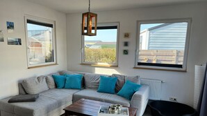 A modern living room with a grey sectional sofa, a wooden coffee table, and large windows offering a view of the outdoors.