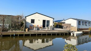 A waterfront mobile home with a dock, a small boat, and a clear blue sky.