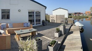 A waterfront property with a wooden deck, outdoor seating, and a small shed.