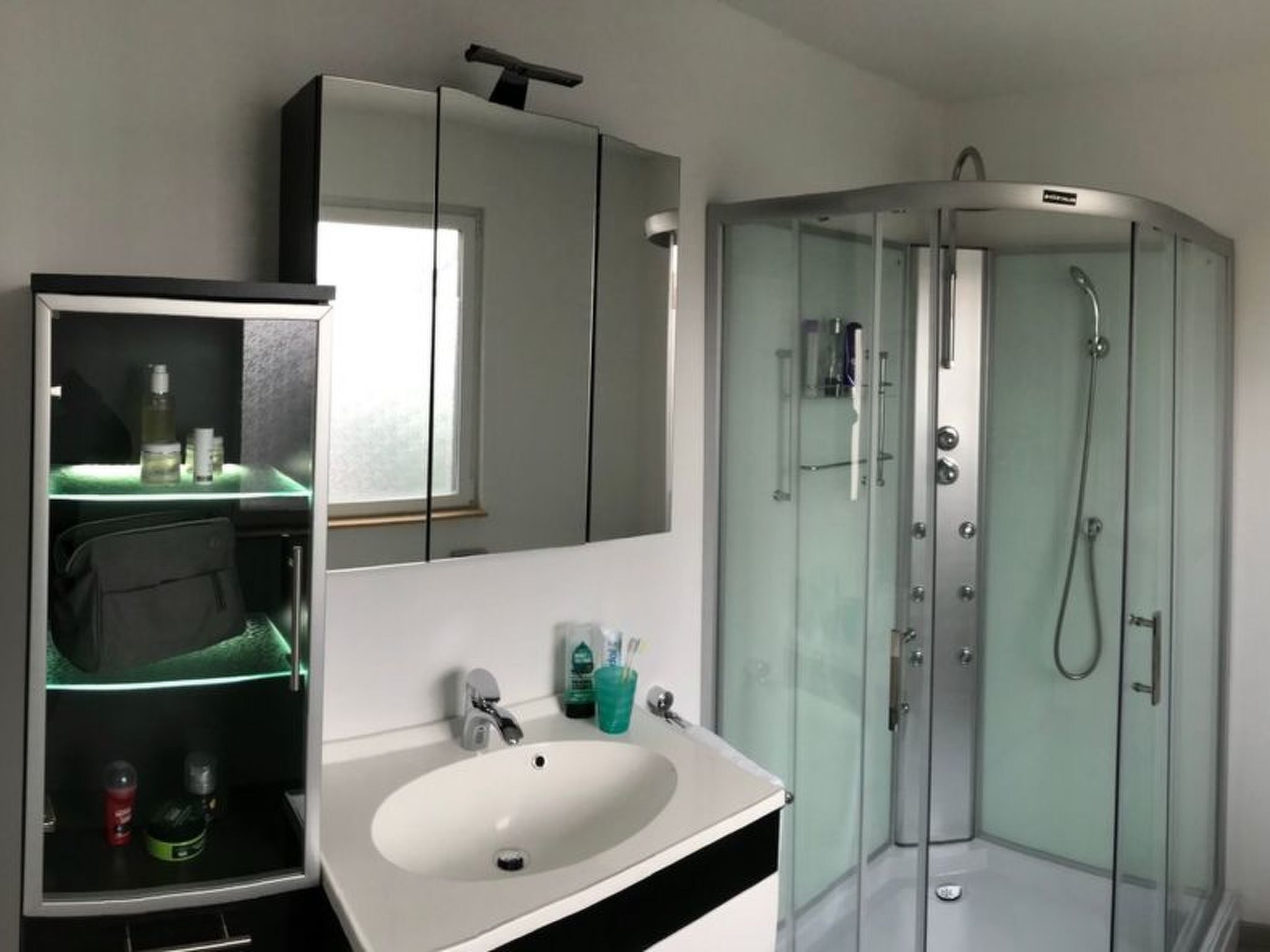 A modern bathroom with a glass-enclosed shower, a white sink with a mirror above it, and a glass shelf with toiletries.