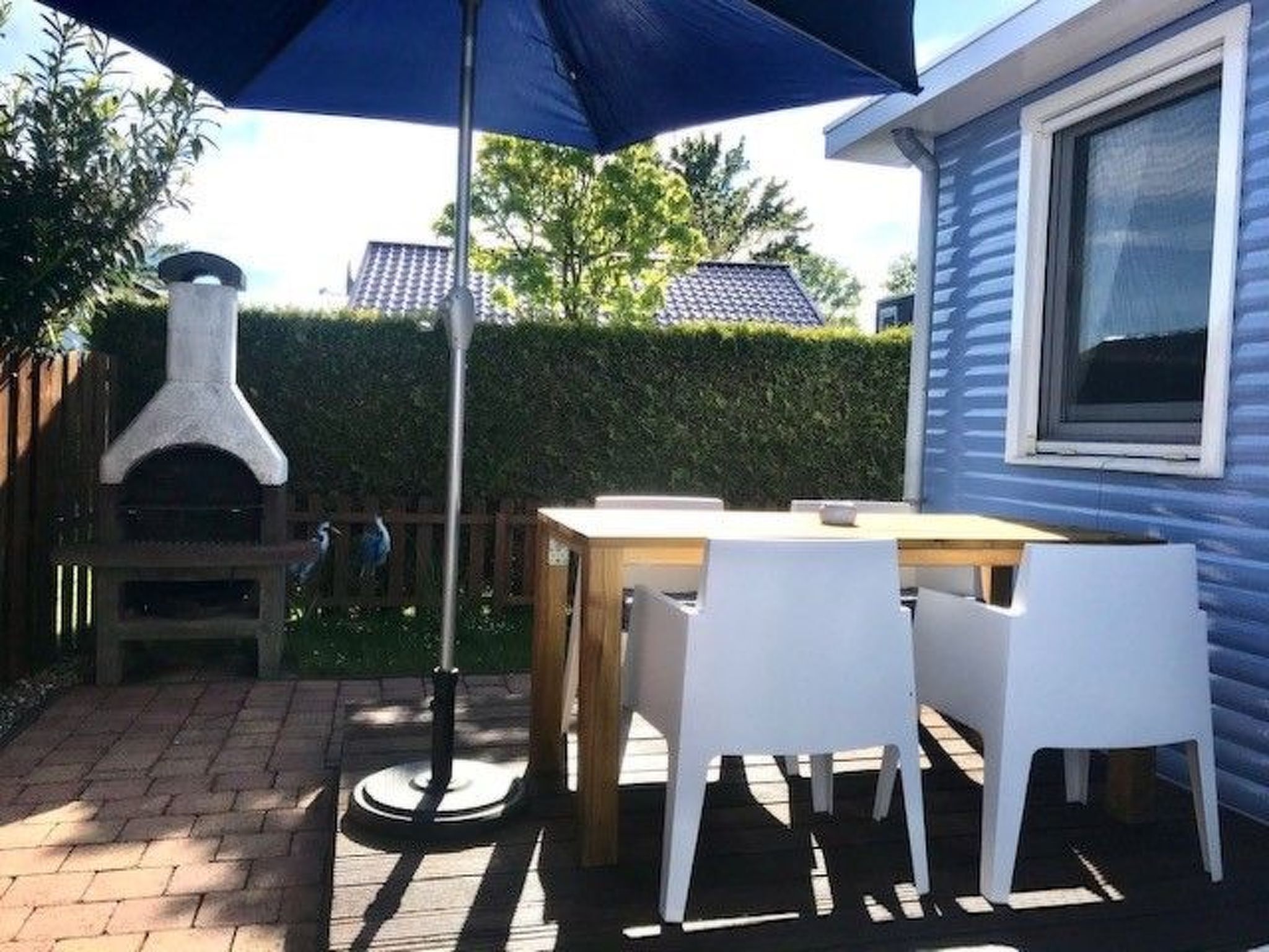 Eine Terrasse im Freien mit Tisch und Stühlen, einem Grill und einem blauen Sonnenschirm.