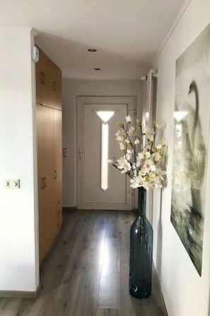 A hallway with wooden flooring, a door at the end, a vase with flowers, and a painting on the wall. - Haus DE BLAUWE REIGER by Interhome (Wervershoof)