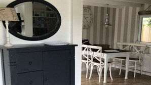 Una habitación con un armario azul oscuro, un espejo redondo, una mesa de comedor con sillas blancas y una pared a rayas.
