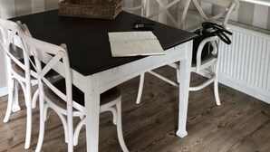 Un comedor con una mesa negra, sillas blancas, pared a rayas, un reloj y una ventana con vistas.