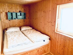 Ein Zimmer mit Holzwänden, einem Bett, einem Regal mit Gegenständen und einem Fenster.