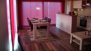 Una cocina compacta con zona de comedor, suelo de madera y un fondo de cortina rosa.