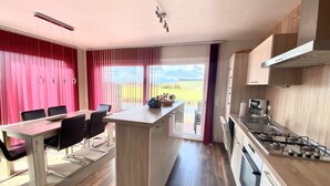 Una cocina moderna con una isla central, un comedor con mesa y sillas, y vistas al exterior.