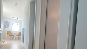 Un couloir au plancher de bois mène à une salle à manger où se trouvent des chaises jaunes et une table.