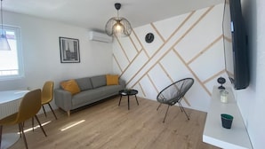 Un salon moderne comprenant un canapé, une table à manger, des chaises, un téléviseur et un mur décoratif.
