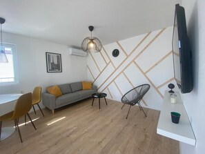 Ein modernes Wohnzimmer mit Sofa, Esstisch, Stühlen, Fernseher und Wanddeko.