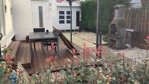 Eine überdachte Terrasse mit Tisch, Stühlen und einem Grill, sowie ein weißes Gebäude im Hintergrund.