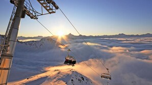 Eine Seilbahn mit Fahrgästen, eine verschneite Berglandschaft und ein Sonnenaufgang.