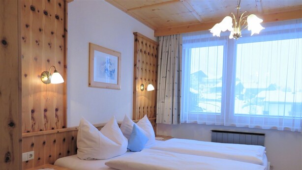 Ein Zimmer mit einem hölzernen Bett, zwei Nachttischen, einem gerahmten Bild an der Wand und einem Fenster mit Vorhängen.