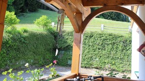 En pergola av trä med utsikt över en välskött trädgård och en häck.