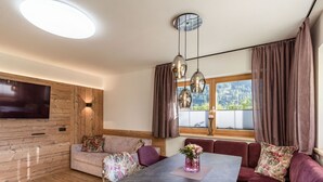 Una sala de estar moderna con una pared de acento de madera, un televisor de pantalla plana, una mesa de comedor con sillas y un sofá con cojines estampados.