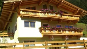 Una casa tipo chalet de dos pisos, con balcones de madera, fachada blanca y una valla de madera al frente.