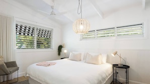 Un dormitorio con una cama grande, dos mesitas de noche, un ventilador de techo y una ventana con persianas.